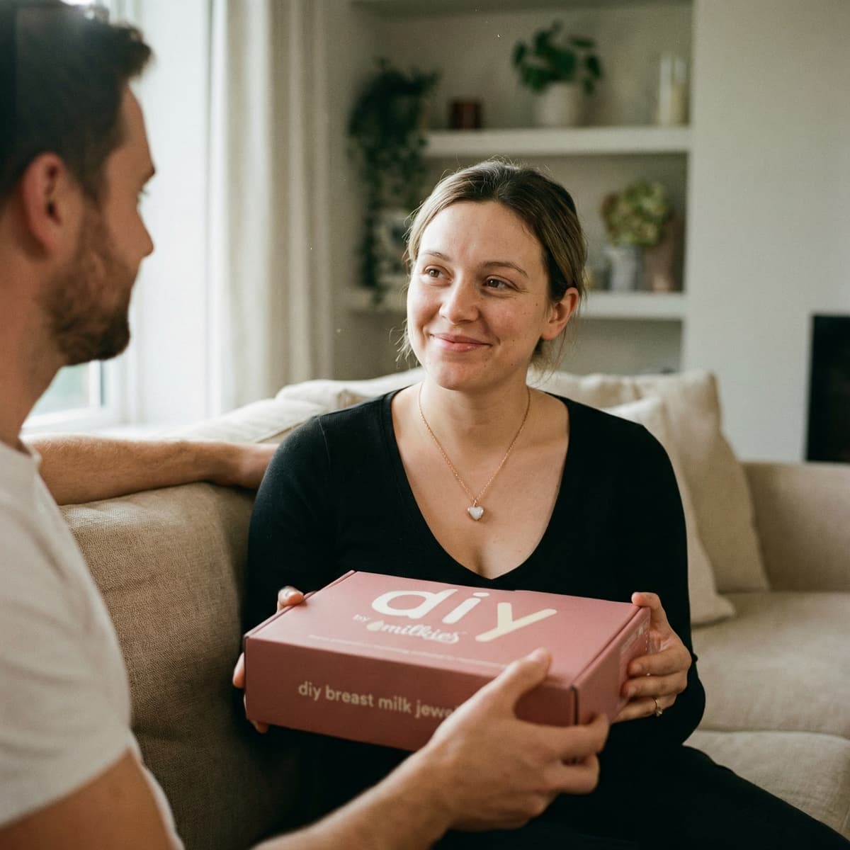 Neue Mama sitzt glücklich auf dem Sofa und freut sich über ein Geschenk für neue Mama: die DIY by MILKIES Box für Breastmilk-Schmuck als persönliche, emotionale Erinnerung zum Selbermachen.