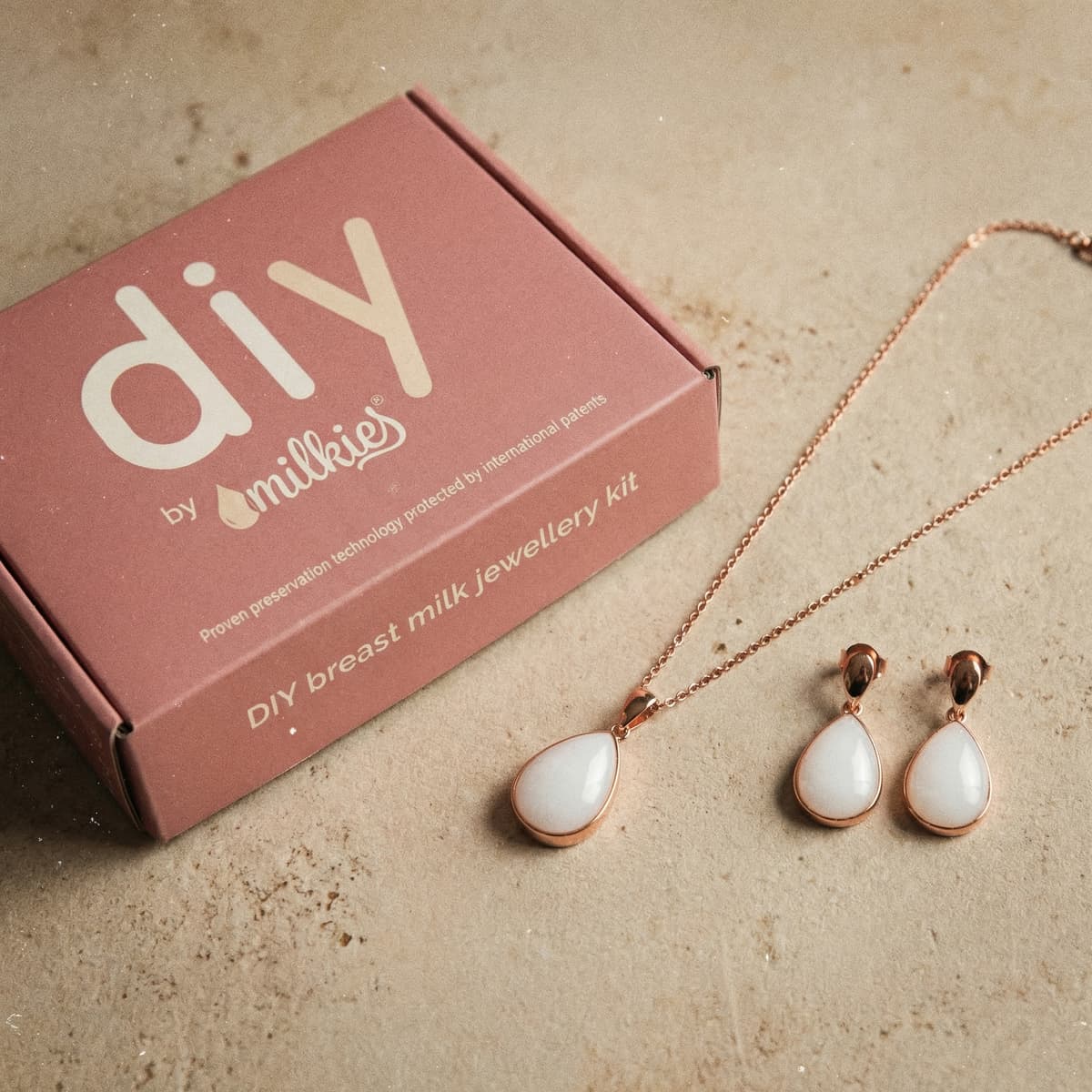 Elegantes Schmuckset als Geschenk für Schwangere: rosegoldfarbene Kette mit passenden Tropfen-Ohrringen im DIY by MILKIES „breast milk jewellery kit“ in rosa Box.