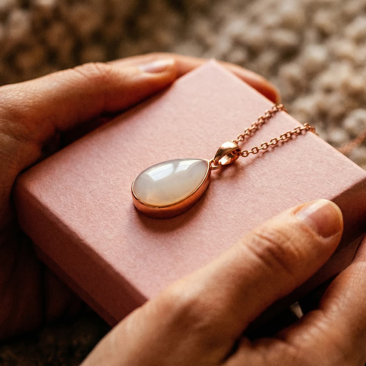 Eine muttermilch halskette als DIY-Erinnerungsstück: Hände halten eine Schmuckbox mit rosegoldener Kette und tropfenförmigem Anhänger – ideal, um das Set sicher und in Ruhe zuhause zu gestalten.