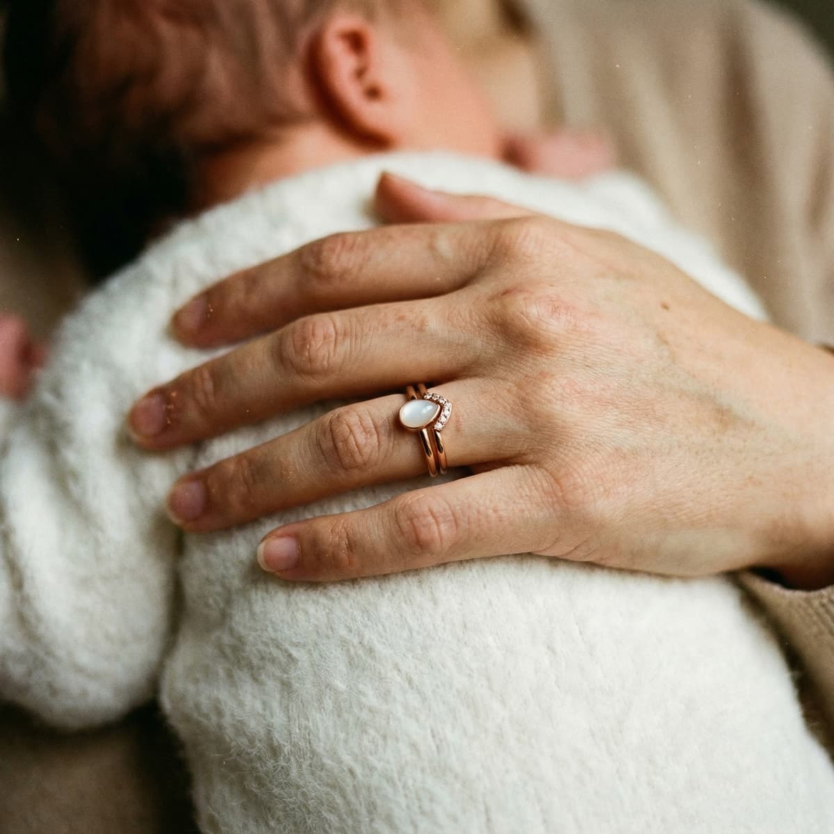 Zärtliche Hand einer Mutter, die ihr Baby hält, während ein eleganter Muttermilch Ring in Roségold als persönliches Andenken glänzt – ideal, um mit dem DIY by MILKIES Kit besondere Momente privat zu bewahren.