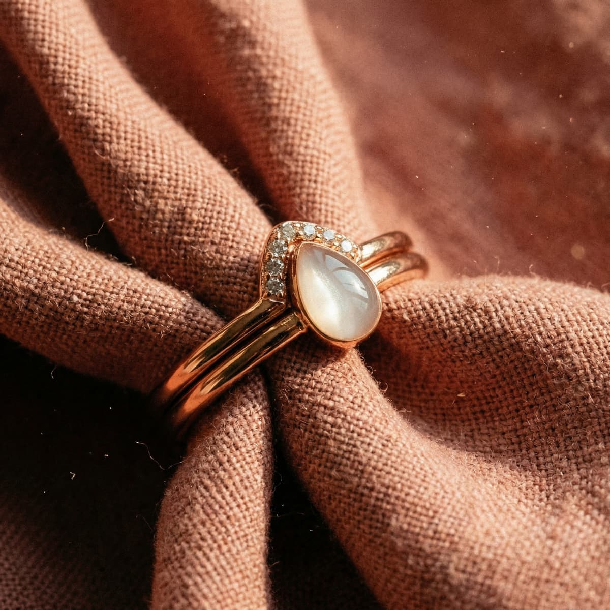 Eleganter Silberring mit milchig-weißem Tropfenstein und funkelndem Halo auf roséfarbenem Stoff – muttermilch ring silber als liebevolles Erinnerungsstück.