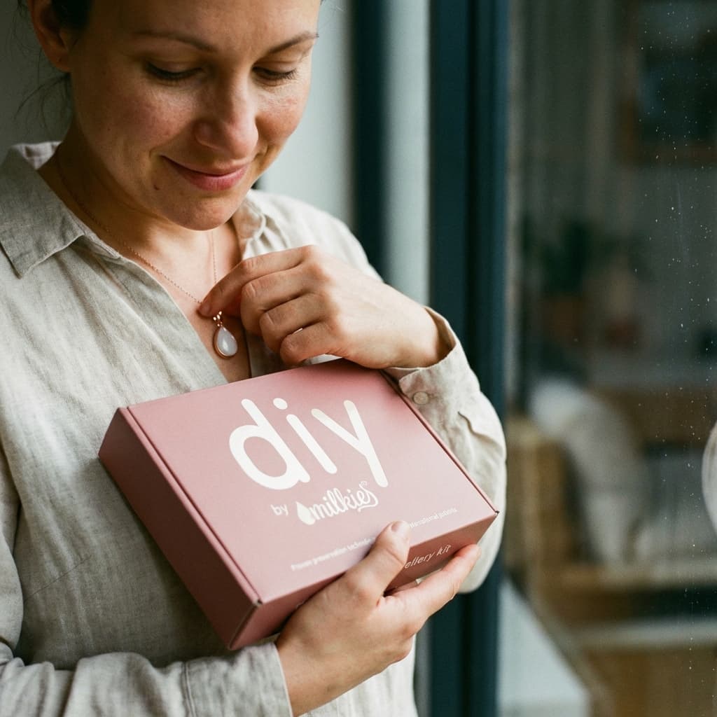 Frau hält das DIY by MILKIES Kit in den Händen und zeigt eine zarte Muttermilchkette DIY als persönliches Erinnerungsstück – ideal, um das Schmuckstück zuhause selbst zu gestalten.