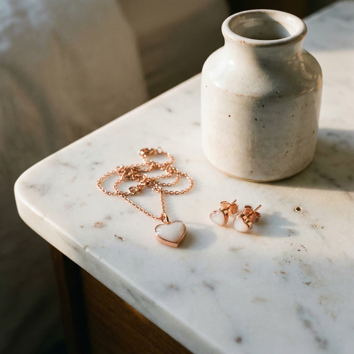 Elegantes roségoldenes Muttermilchschmuck DIY Set mit Herz-Halskette und passenden Herz-Ohrsteckern, milchig-weißer Einsatz, arrangiert auf einer Marmorplatte neben Keramikvase im warmen Licht.