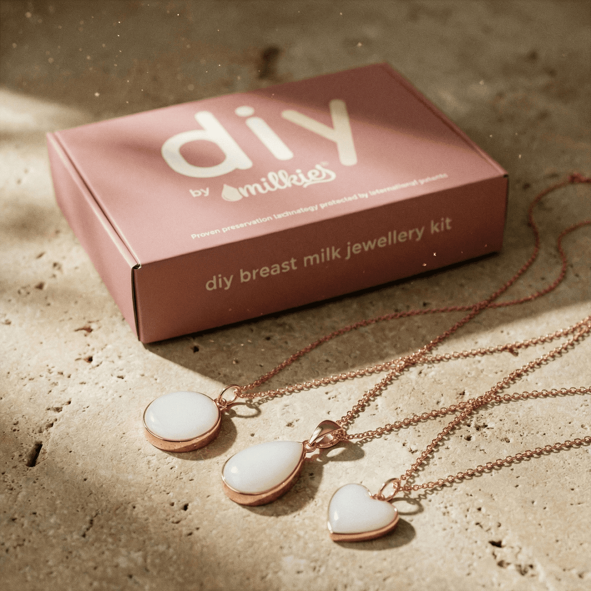 DIY by MILKIES Box mit roségoldfarbenen Kettenanhängern in Herz-, Tropfen- und Rundform auf Steinoberfläche, Teil eines Set DIY Muttermilch Kette für die Herstellung einer Muttermilchkette zuhause