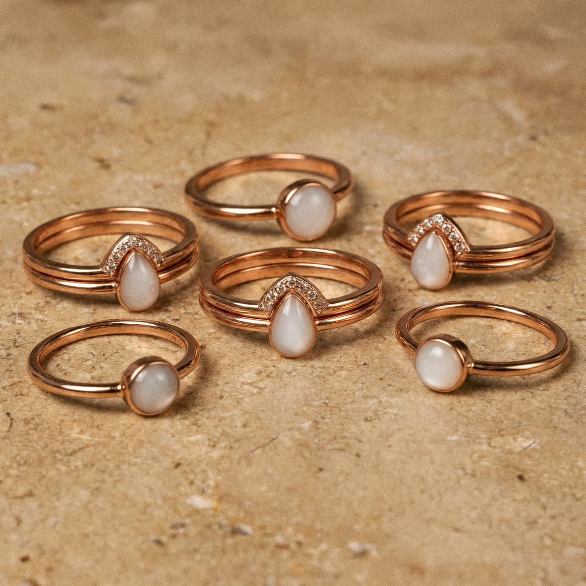 Elegante Roségold-Ringe mit milchig-weißen Tropfen- und Rundsteinen auf Steinuntergrund, ideal als Set Muttermilchring DIY für personalisierte Erinnerungsstücke.
