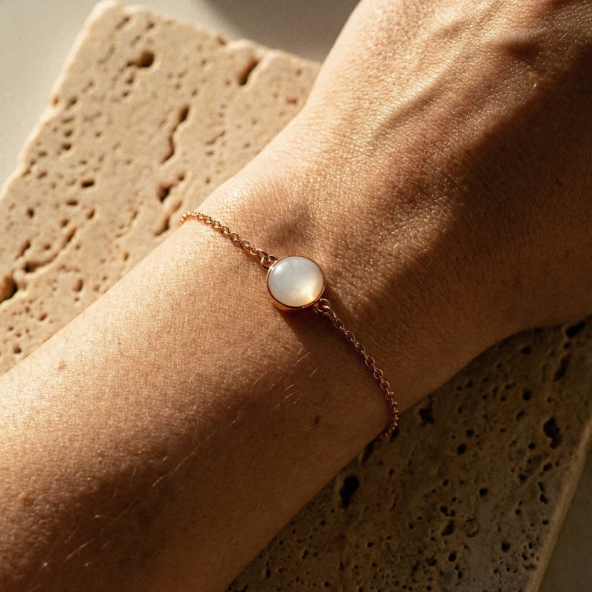 Nahaufnahme eines zarten roségoldenen Kettenarmbands am Handgelenk mit milchig-weißem Cabochon, inspiriert davon, ein Armband aus Muttermilch selbst machen zu können.