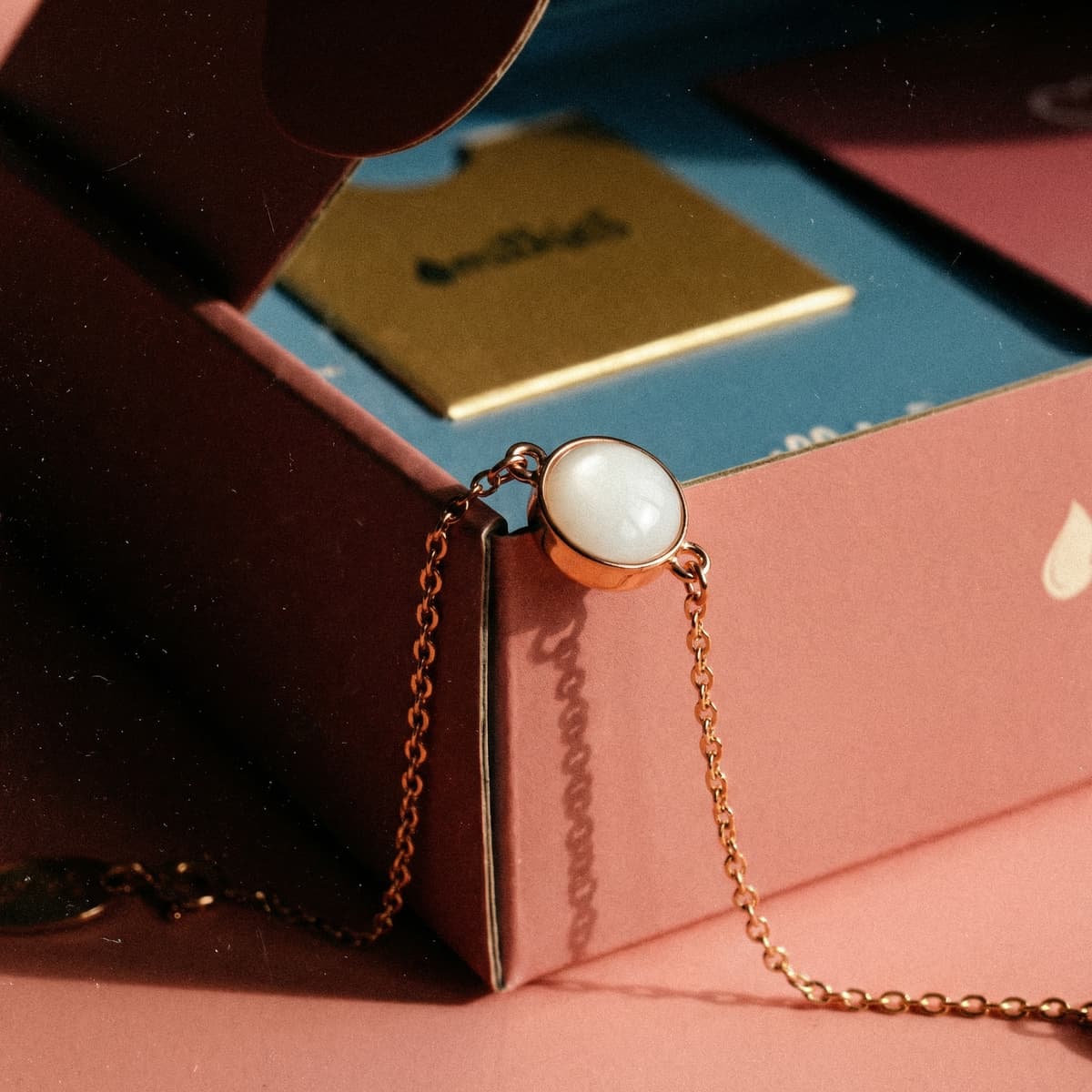 Elegantes roségoldenes Armband mit rundem, milchig-weißem Stein auf rosafarbener Box – Inspiration, wie man ein Armband mit Muttermilch selber machen kann.