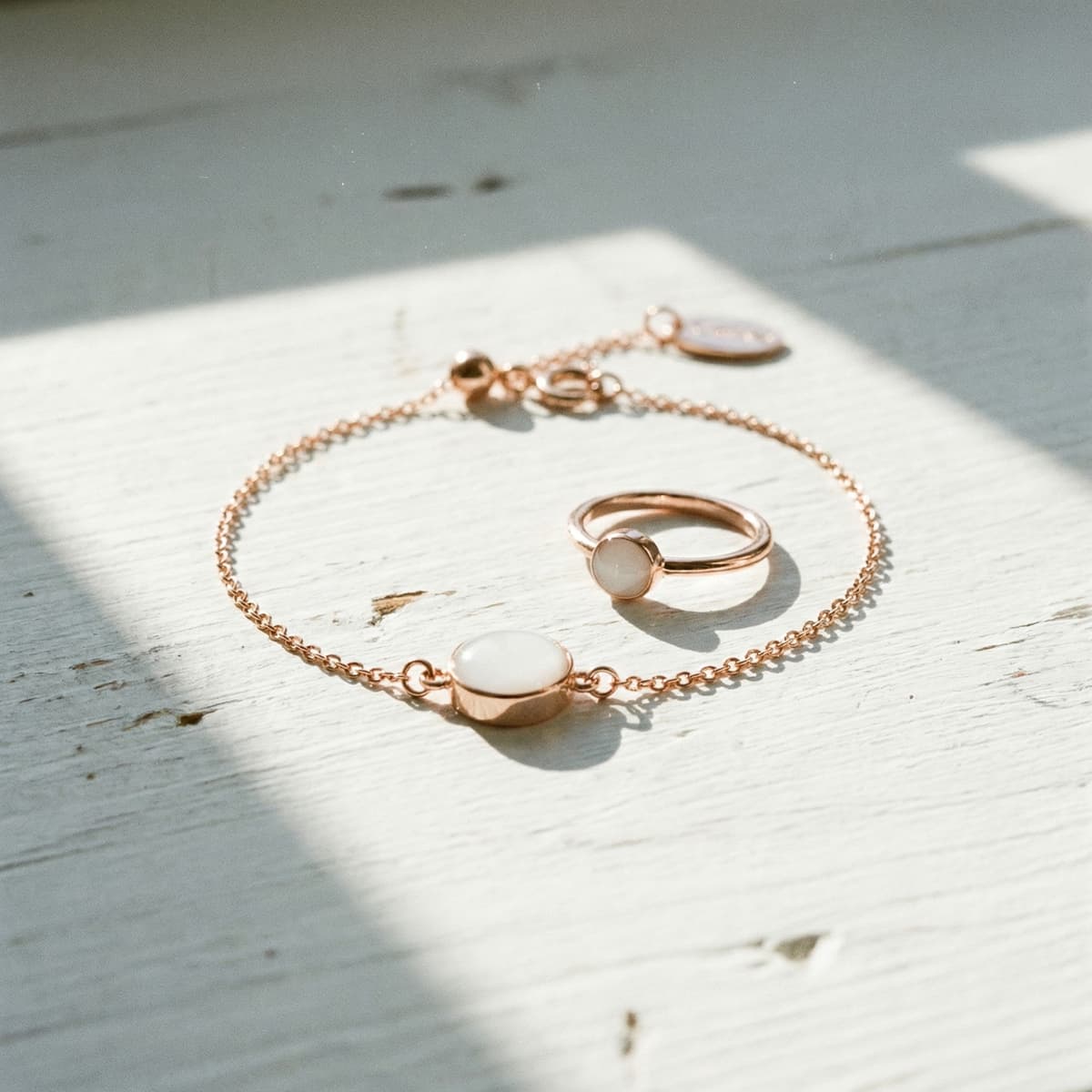 Roségoldenes Armband mit ovalem, milchig-weißem Cabochon als DIY Muttermilch Armband, daneben ein passender Ring auf hellem Holztisch im Sonnenlicht.