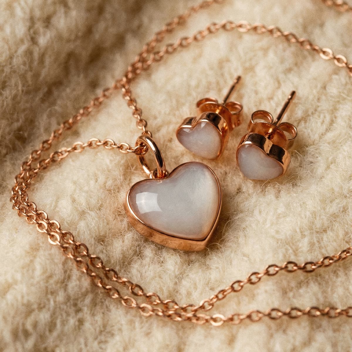 Elegantes roségoldfarbenes Herz-Schmuckset mit Kette und passenden Ohrsteckern auf cremefarbenem Stoff, ideal als Geschenk zum Ende der Stillzeit und persönliches Erinnerungsstück.
