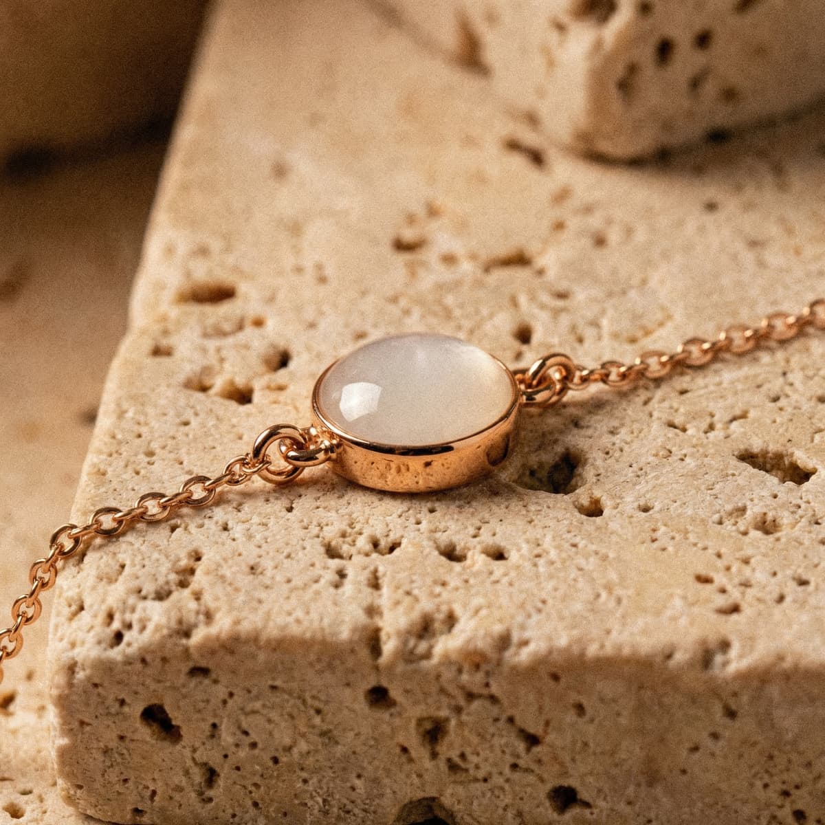 Elegantes roségoldfarbenes Muttermilch Armband mit zarter Kette und ovalem, milchig-weißem Cabochon auf hellem Naturstein als Erinnerungsstück an die Stillzeit.