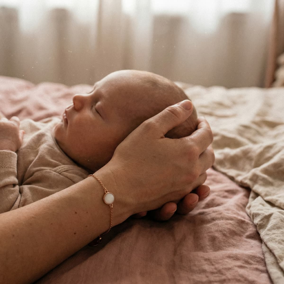 Schlafendes Baby, dessen Hand sanft gehalten wird; am Handgelenk ein zartes Erinnerungsarmband – ein Muttermilch Armband Bastelset als DIY-Idee, um besondere Momente zuhause persönlich festzuhalten.