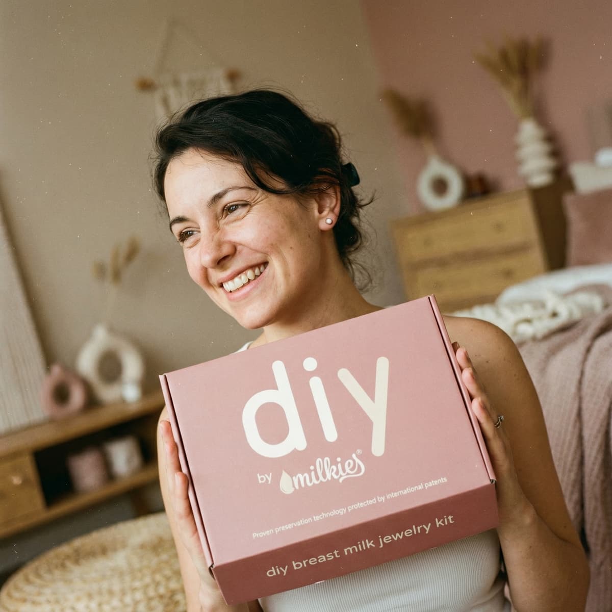 Lächelnde Mutter hält das DIY by MILKIES Set in den Händen – ideal, um Muttermilch Ohrringe selber machen zu können und ein persönliches Erinnerungsstück sicher zuhause zu gestalten.