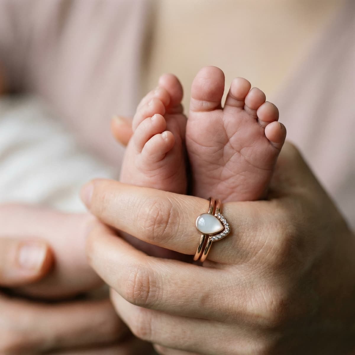 Nahaufnahme von Babyfüßchen in der Hand der Mutter mit roségoldenem Ring und milchig-weißem Herzstein als zartes Stillandenken.